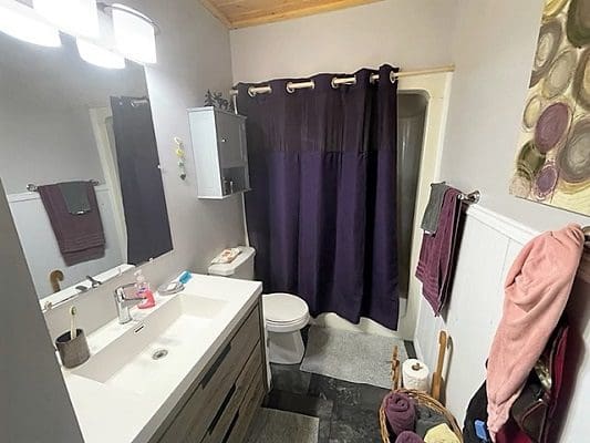 A bathroom with a purple shower curtain and sink.