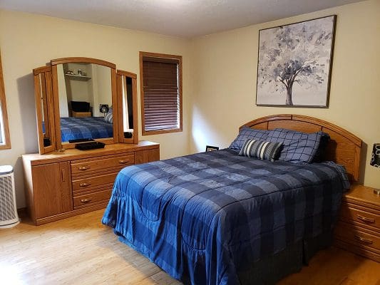 A bedroom with a blue comforter and dresser.