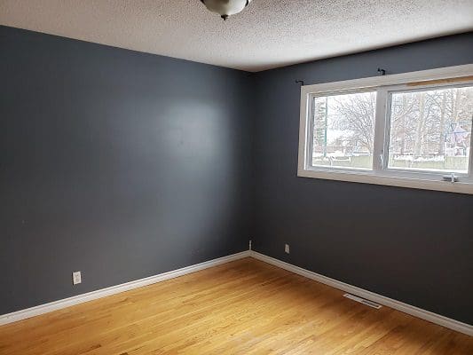 An empty room with gray walls and hardwood floors.