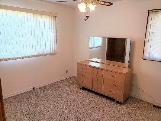 An empty room with a dresser and ceiling fan.