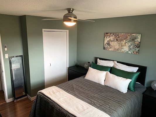 A bedroom with green walls and a ceiling fan.