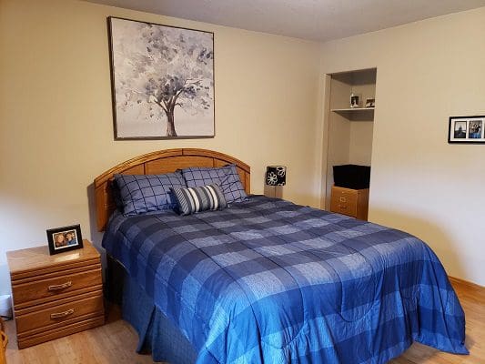 A bedroom with a blue comforter and a picture on the wall.