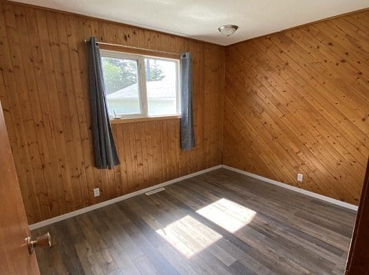 An empty room with wood paneling and a window.