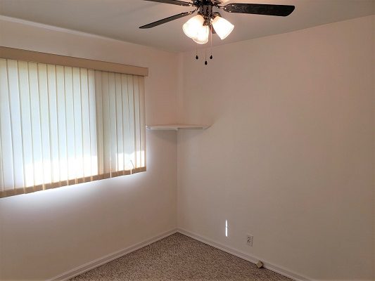 An empty room with a ceiling fan and a window.