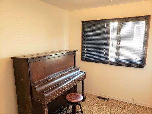 An old piano sits next to a window in a room.