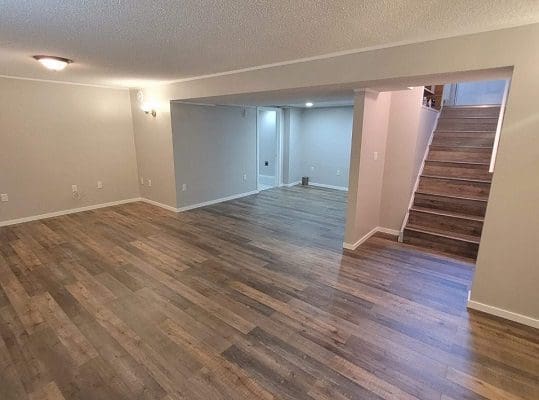 Empty living room with hardwood floors and stairs.