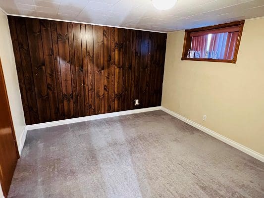 An empty room with wood paneling and a carpet.