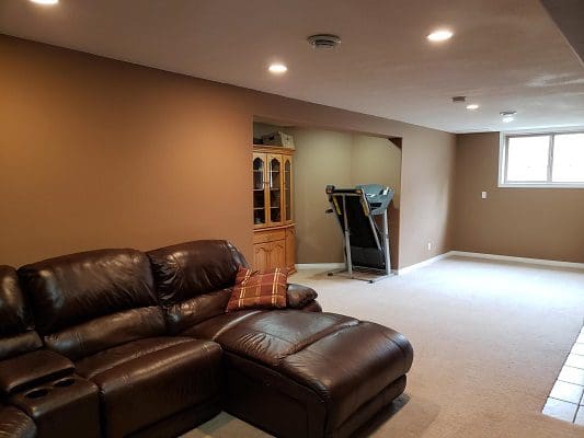 A living room with brown leather furniture and a treadmill.