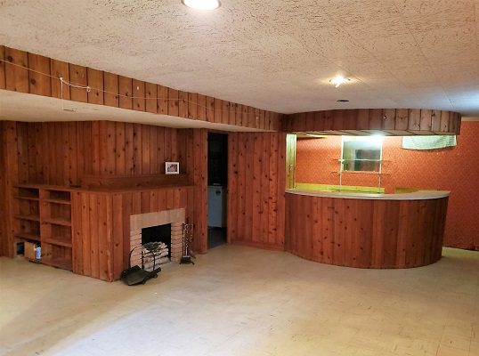 An empty basement with wood paneling and a fireplace.