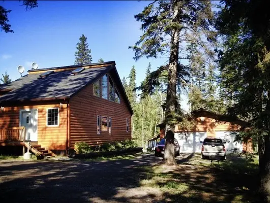 A log cabin in the woods with a car parked in front of it.