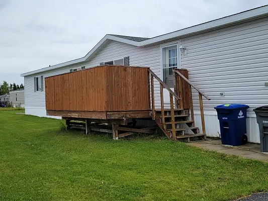 A mobile home with a wooden deck and a trash can.