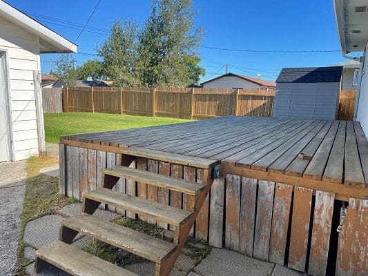 A backyard with a wooden deck and steps leading to a backyard.