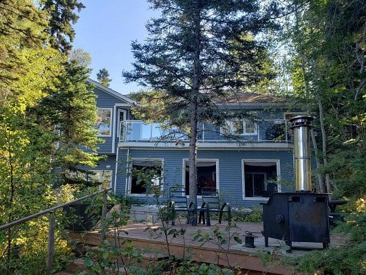 A house in the woods with a grill on the deck.