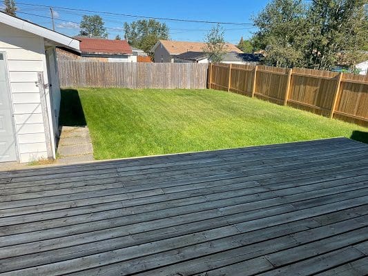A backyard with a wooden deck and grass.