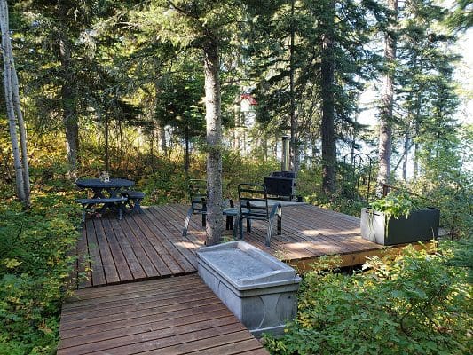 A deck in the woods with a table and chairs.