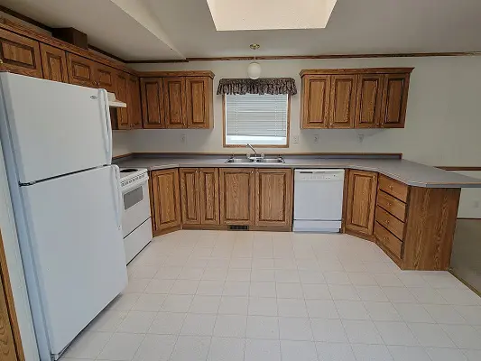 An empty kitchen with wood cabinets and white appliances.