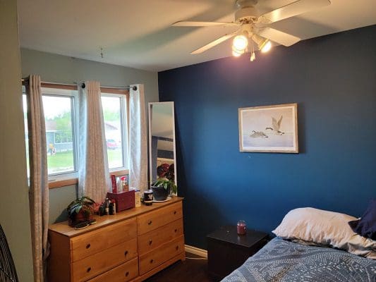 A bedroom with blue walls and a ceiling fan.