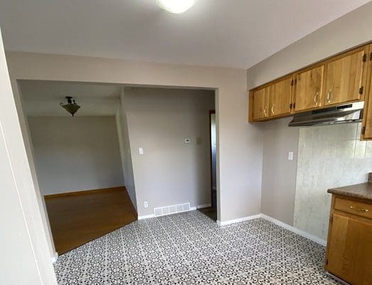 An empty kitchen with white cabinets and a tile floor.