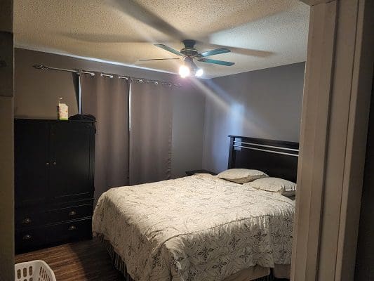 A bedroom with a bed, dresser and ceiling fan.