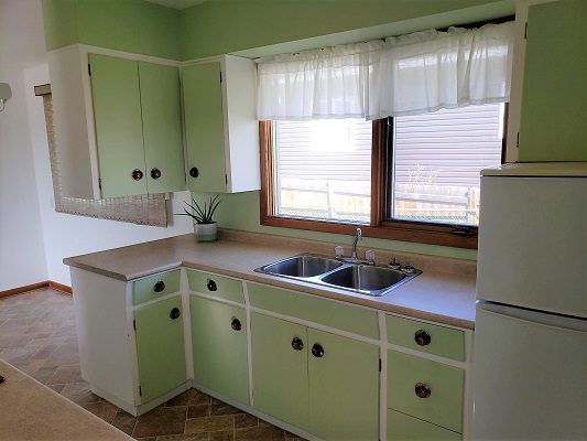 A kitchen with green cabinets and white counter tops.