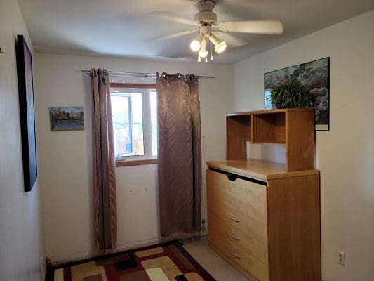 A bedroom with a dresser and a ceiling fan.