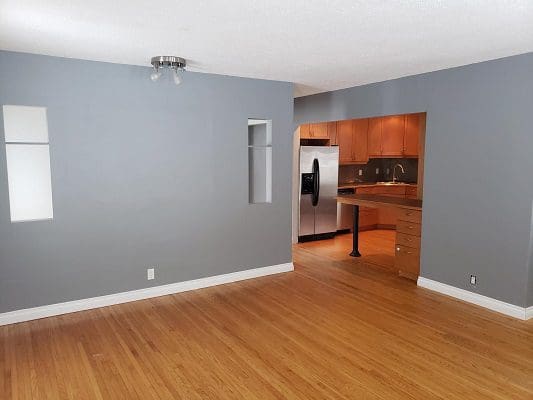 An empty living room with gray walls and hardwood floors.
