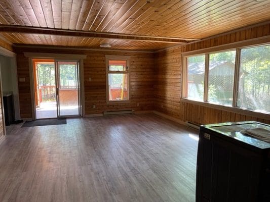 An empty living room with wood paneling and windows.