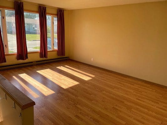 Empty living room with hardwood floors and windows.