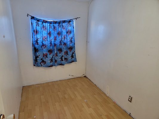 An empty room with a wooden floor and a blue curtain.