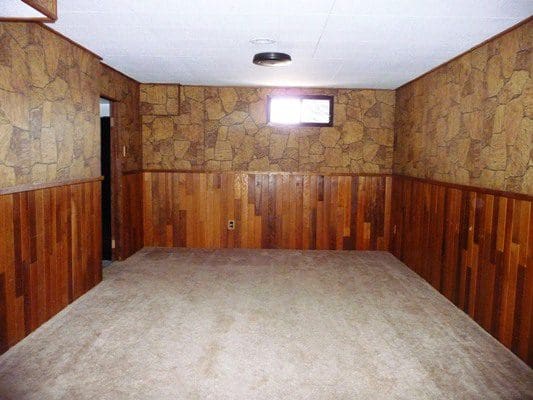 An empty room with wood paneling and carpet.