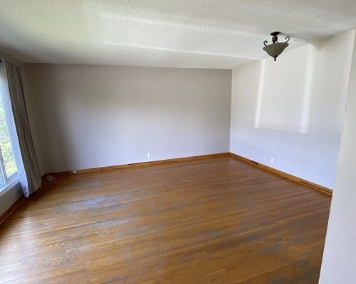 Empty living room with hardwood floors and a ceiling fan.