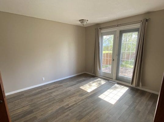 An empty room with hardwood floors and a sliding glass door.
