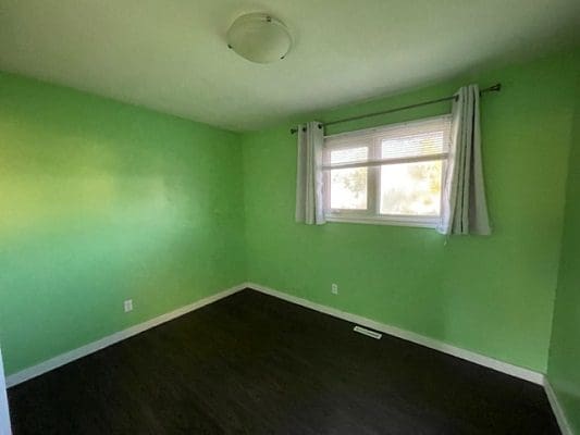 A green room with hardwood floors and a window.