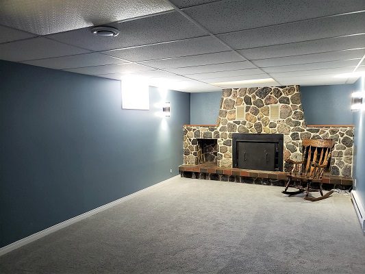 An empty basement with a rocking chair and fireplace.