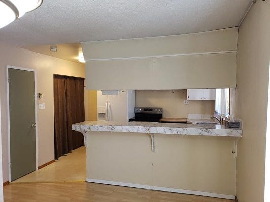 An empty kitchen with wood floors and a refrigerator.