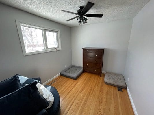 A room with a bed, dresser and a ceiling fan.