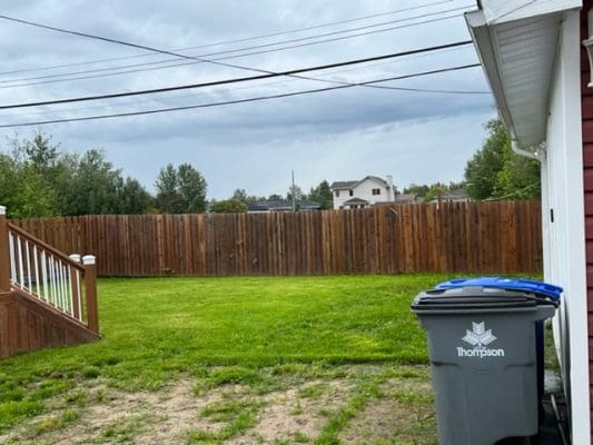 A backyard with a trash can and a fence.