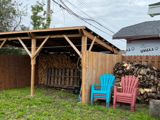 A wooden shed with chairs and a pile of wood.