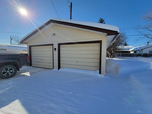 A truck is parked next to a garage in the snow.