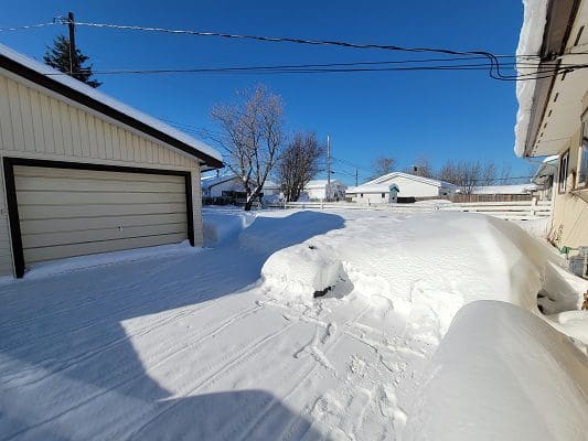 A driveway covered in snow with a car parked in it.