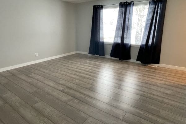 An empty room with wood floors and curtains.