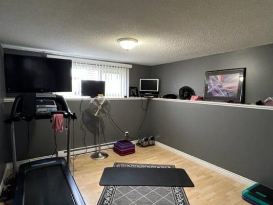 A gym room with a treadmill and a tv.
