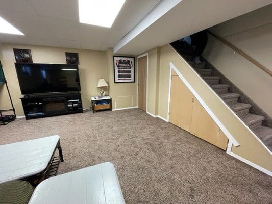 An empty living room with stairs and a tv.
