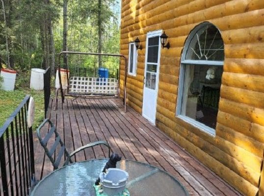 The deck of a log cabin with a table and chairs.