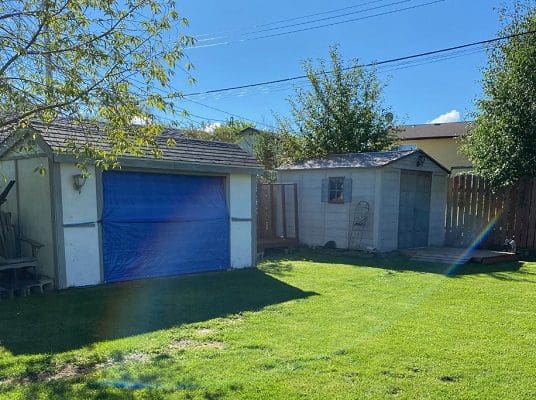 A backyard with a blue garage and a blue shed.