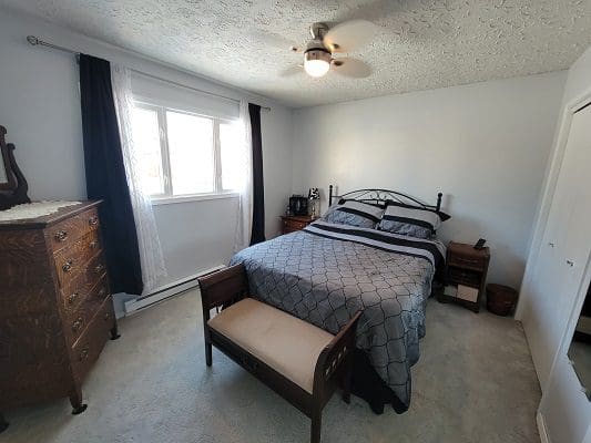 A bedroom with a bed, dresser and ceiling fan.