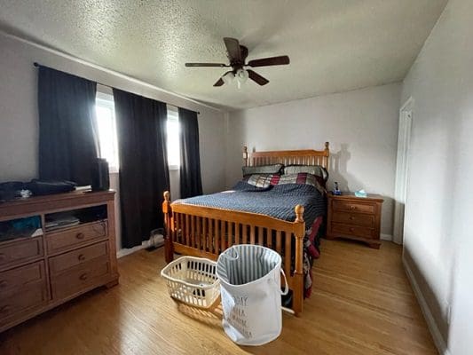 A bedroom with hardwood floors and a ceiling fan.