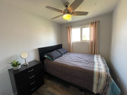 A bedroom with a bed, dresser and ceiling fan.