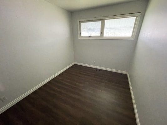 An empty room with hardwood floors and a window.