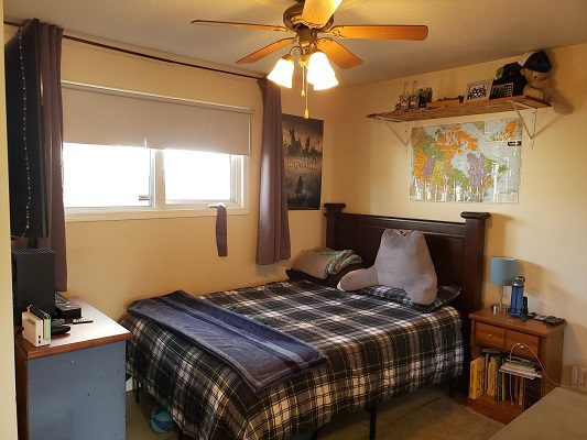 A bedroom with a plaid blanket and a fan.